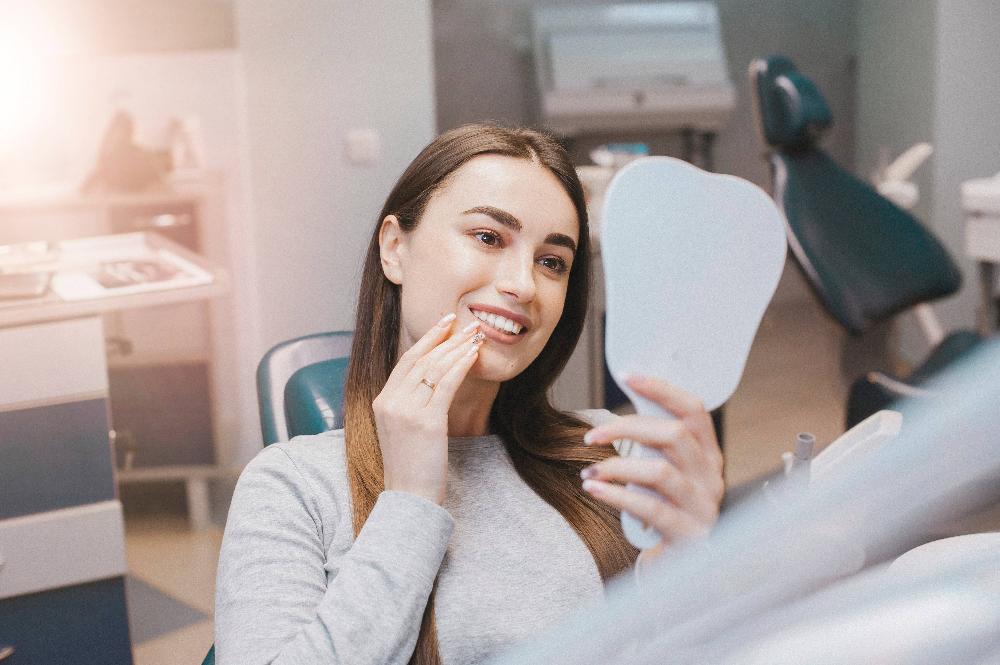A woman smiling while checking her teeth after a Same-Day Crowns in Rockville, MD